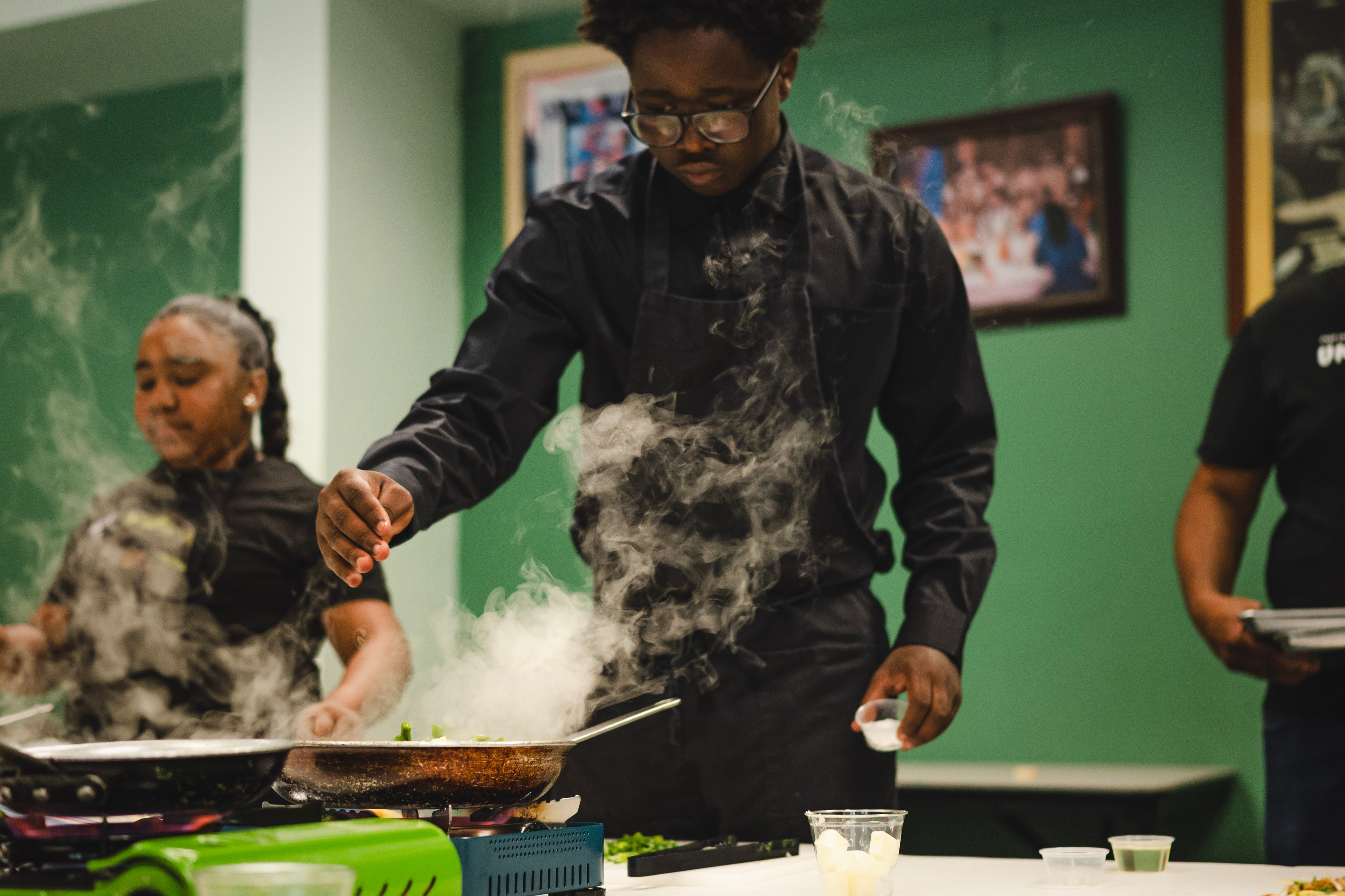 Student seasoning a sizzling pan with steam rising