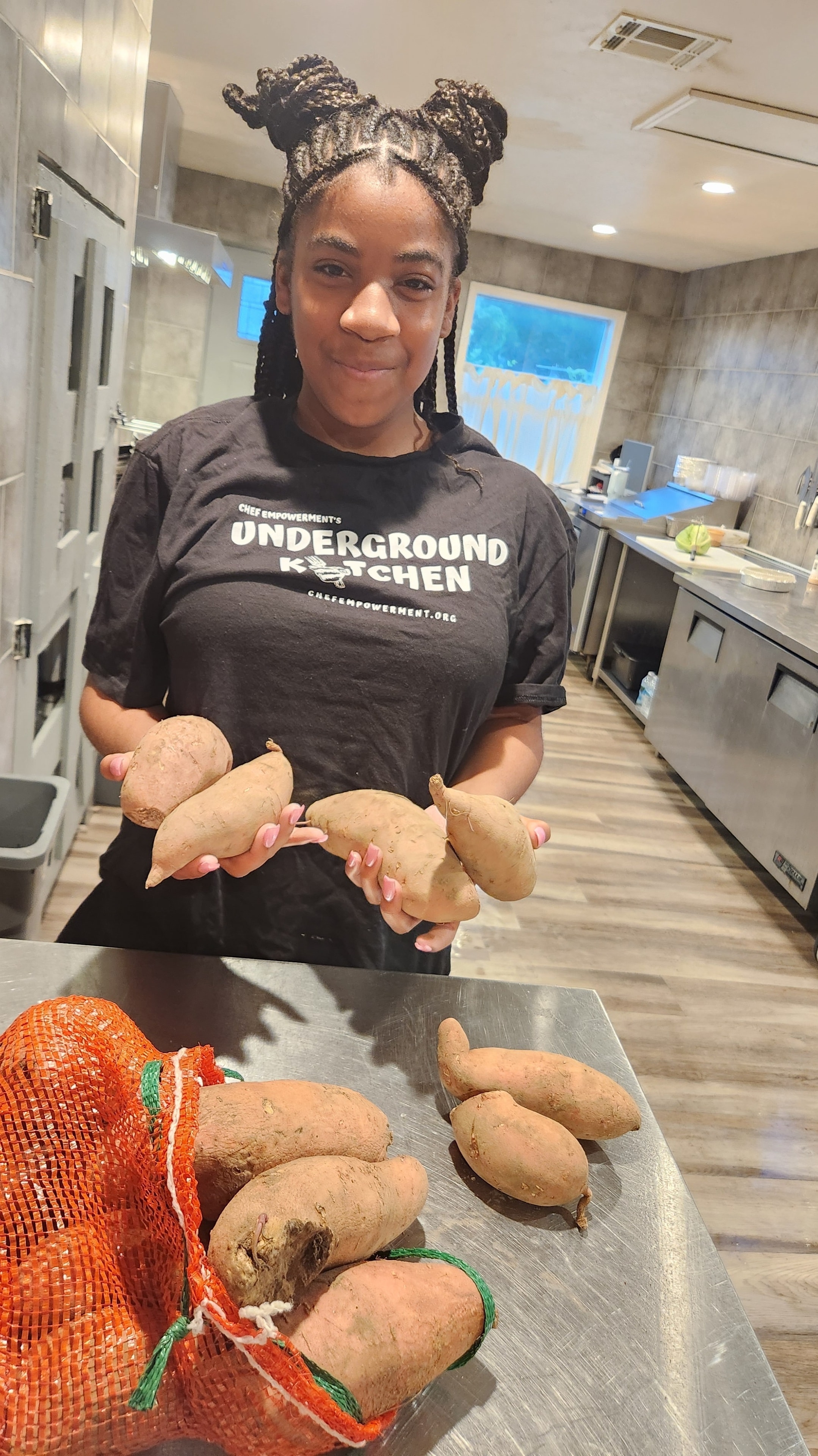 Underground Kitchen student holding fresh sweet potatoes in the kitchen