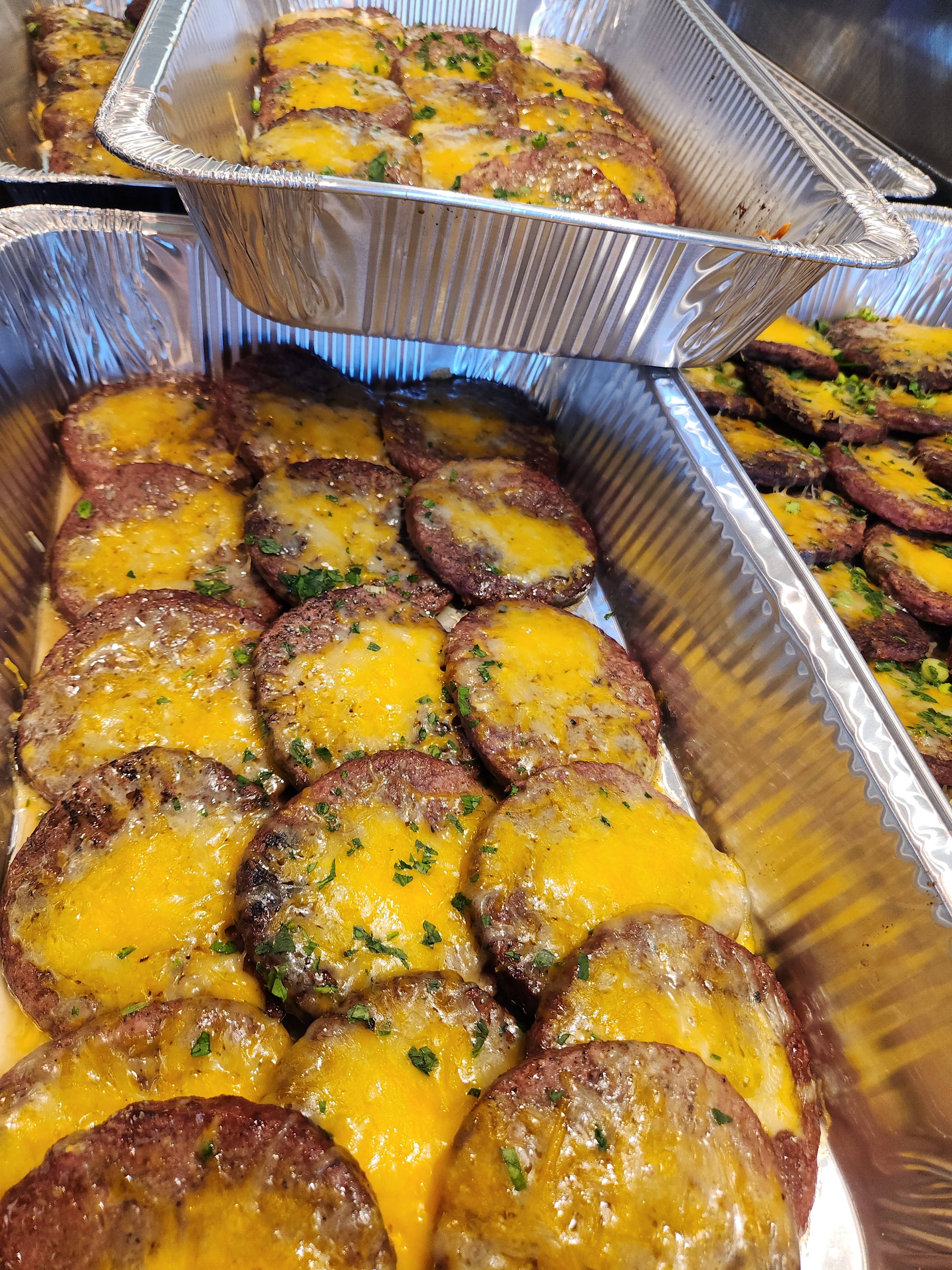 Cheeseburger patties in aluminum trays ready for service